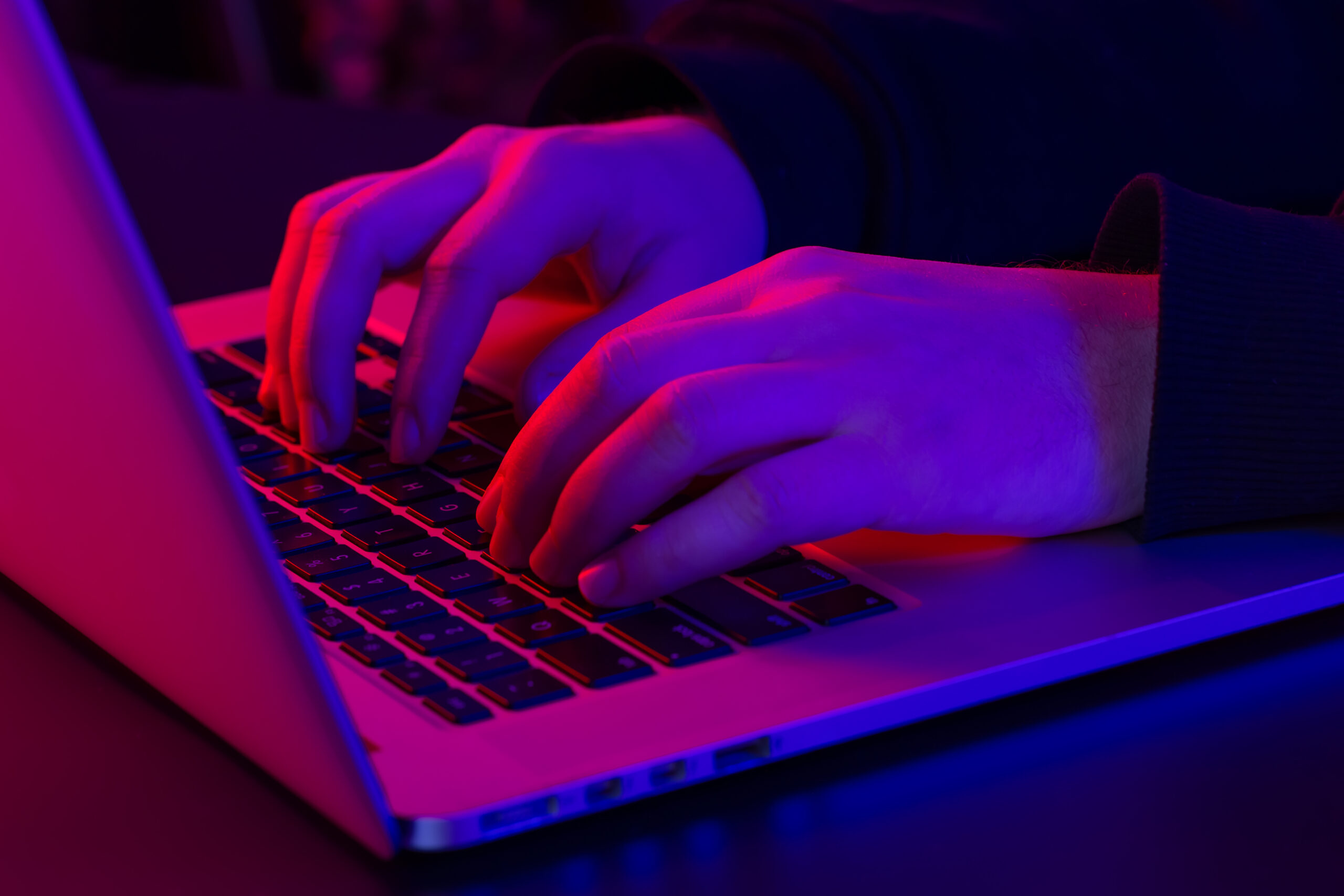 A man uses a laptop, close-up, male hands in neon lighting, the concept of working at night.